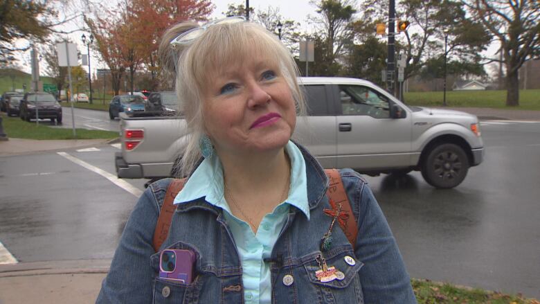 A woman wearing a jean jacket and a aqua blue shirt speaks to a reporter near a crosswalk.