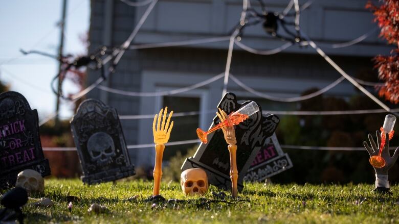 Decorations of a skeleton rising from the ground holding a plastic cup, along with gravestones, in a front yard.