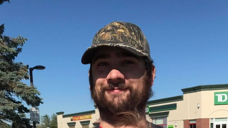 A man in a hat and a beard stands outside.