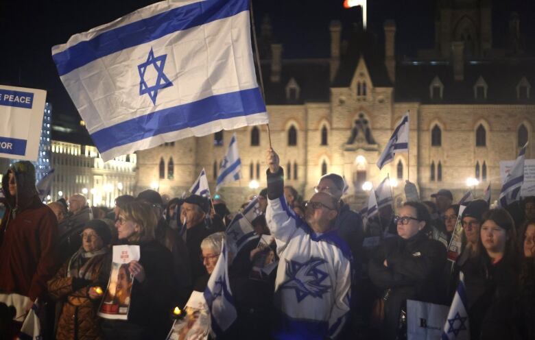 People wave white and blue flags with a blue star during a rally at night at a legislature.