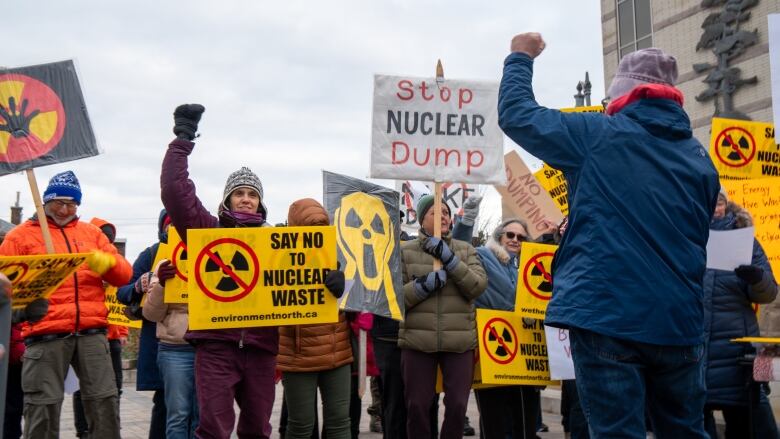 A group of people hold yellow signs. Two people have their firsts raised in the air.