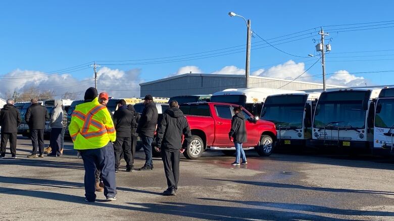 Workers stand outside CBRMs transit hub. They are next to busses and Handi-Trans vehicles. 