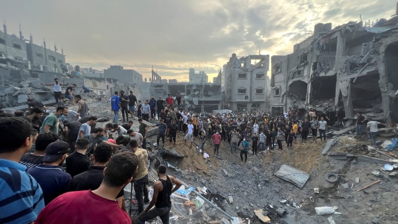 A crowd of people are seen amid the rubble of destroyed buildings.