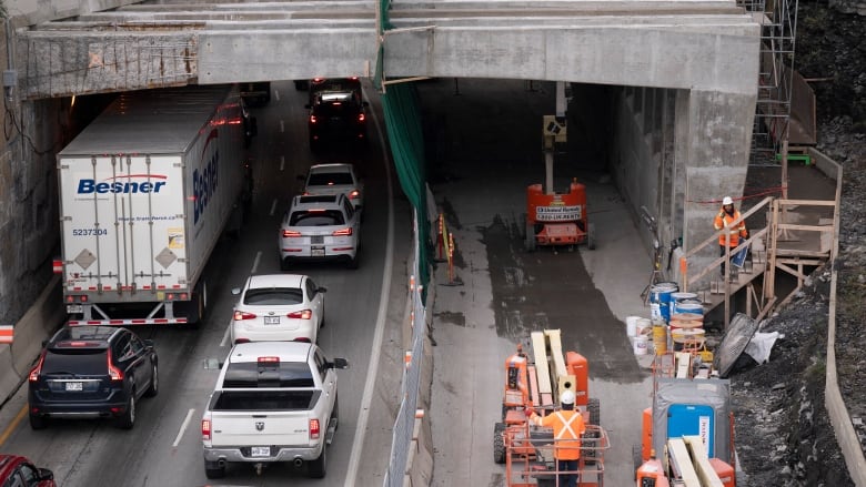 Cars lined up in front of a tunnel. In another lane, construction vehicles.