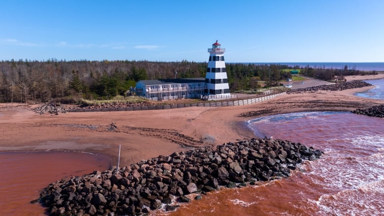 A pile of rocks on a beach in front of a lighthouse 