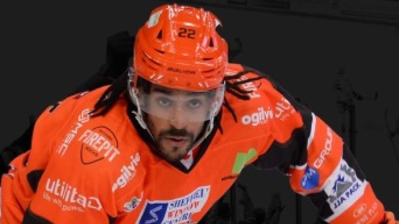 An intense hockey player in action, wearing a bright orange helmet and jersey. 