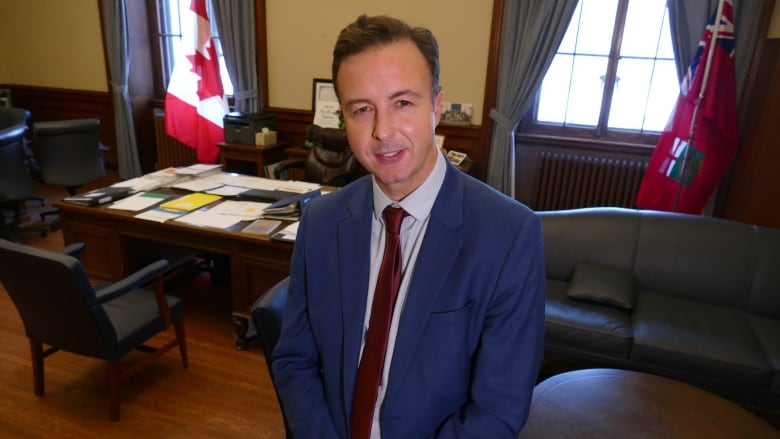 A man in a suit stands in an office.