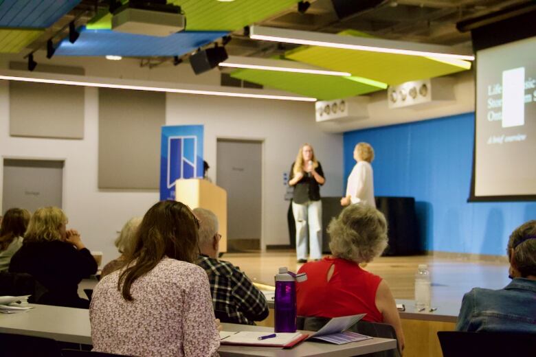 People sit and listen to two others speaking on a stage. 