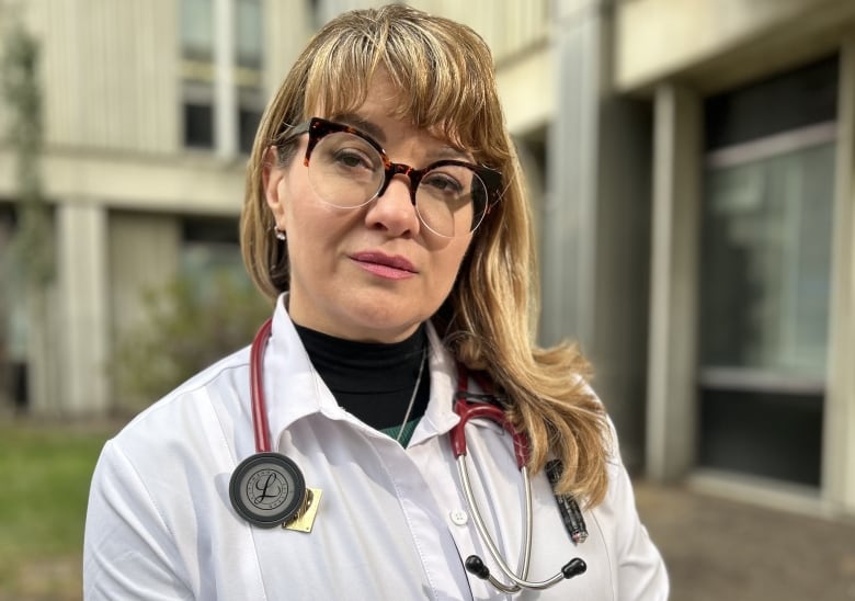 Female physician in white coat and stethoscope standing outside.