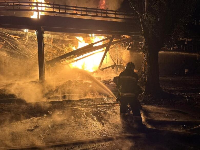 Firefighters are seen from behind spraying a hose into a burning structure