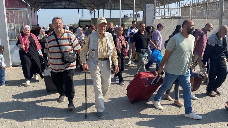 Dozens of people pulling suitcases and other belongings walk through a border crossing.