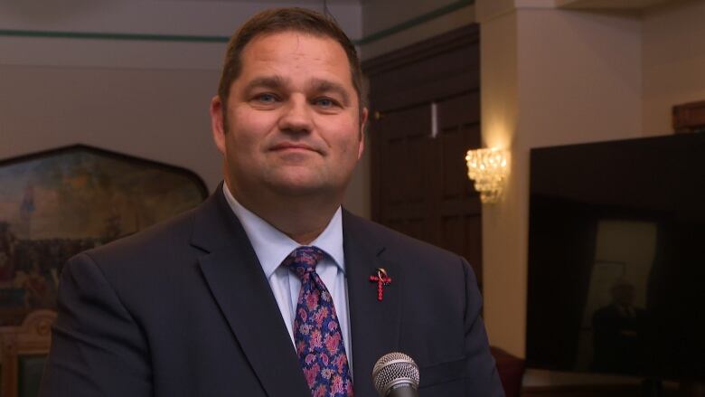 A man wearing a suit smiles in front of a microphone.