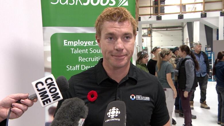 A man with a poppy speaking to microphones.