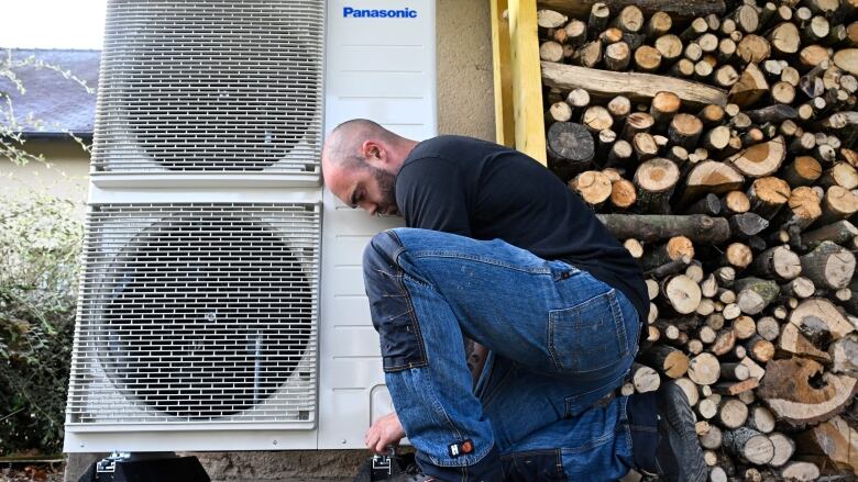 Man kneeling by heat pump and stacks of wood