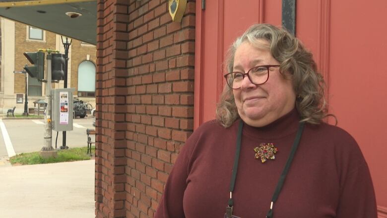 Darlene Harris stands by a brick wall smiling in a burgundy shirt. 