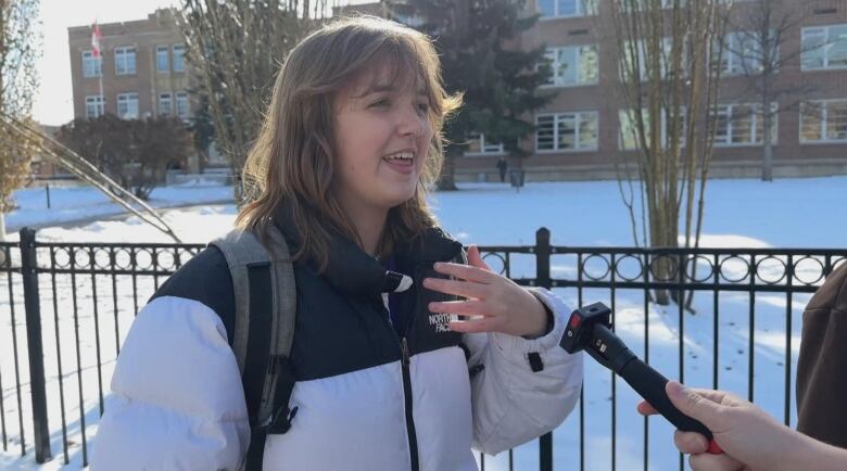 a girl in a white winter coat speaks into a microphone