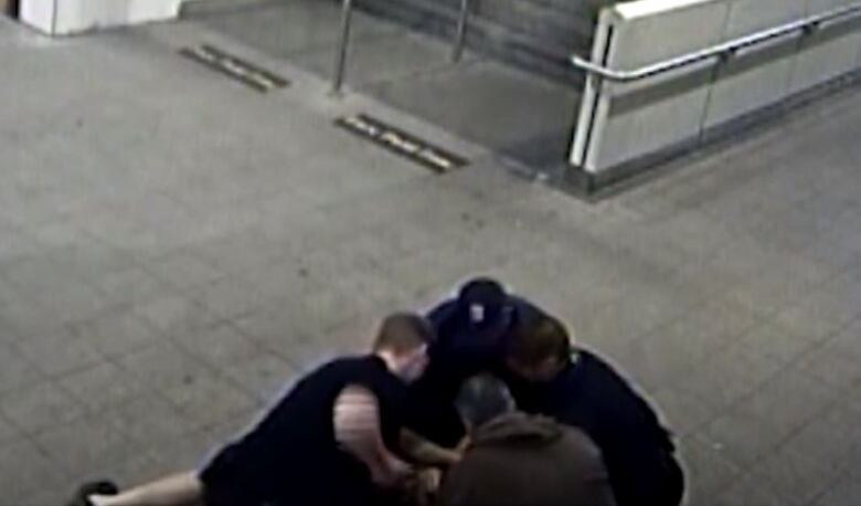 An image taken from grainy CCTV footage shows four police officers crowded in the bottom right corner, holding someone on the ground. One of them can be seen winding up his right arm for a punch. 