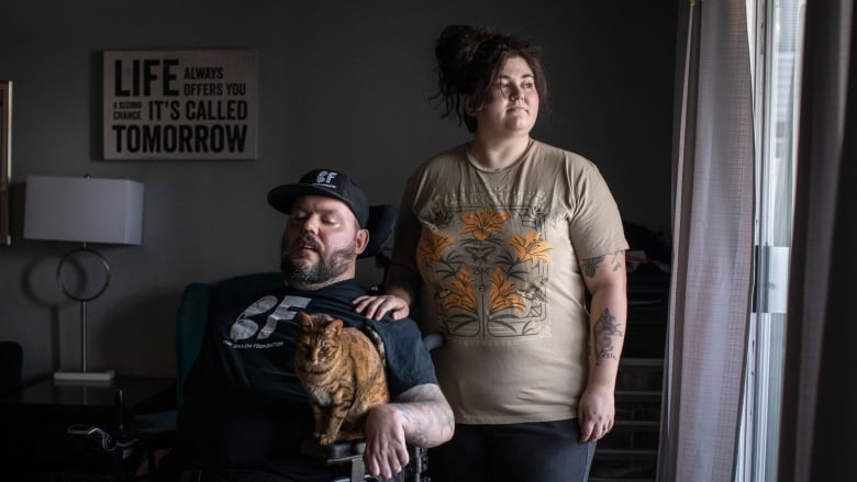 A man in a wheelchair, holding a cat, and a woman pose for a picture.