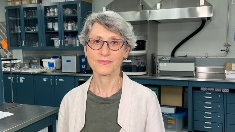 A woman with short hair and glasses poses in a labratory.