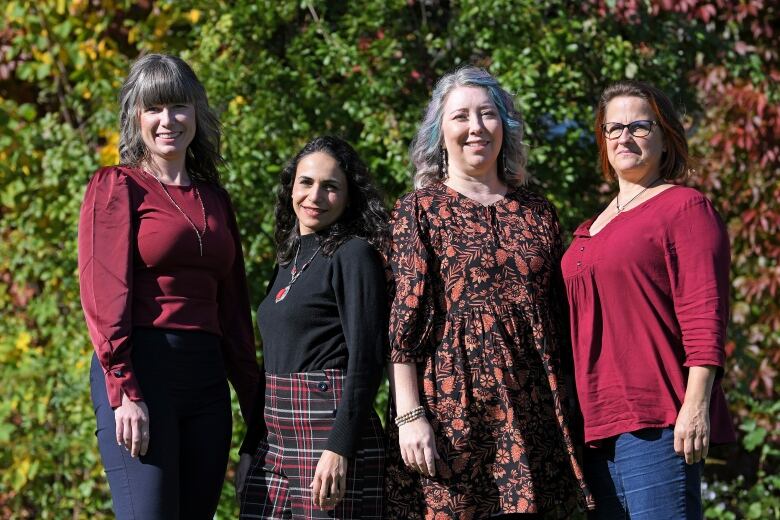 Four people stand together for a photo in front of a leafy green backdrop.