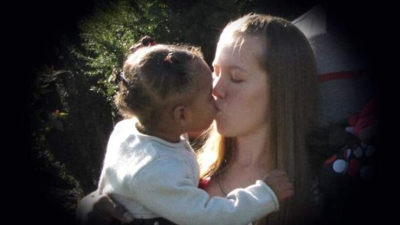 A woman kisses a child she's holding in her arms. 