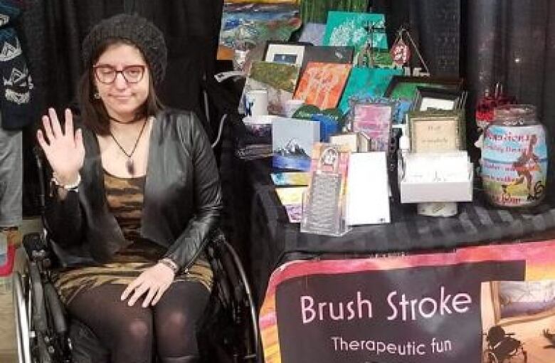 A woman in a wheelchair beside a table filled with artworks.