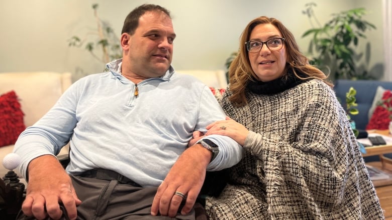 A woman holds a man's hand in a house. They are both sitting down.