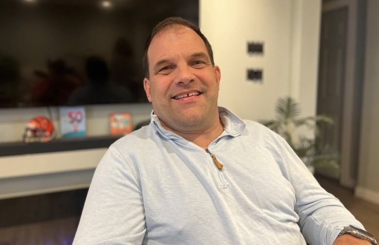 A man smiles while sitting in front of a TV in a home.