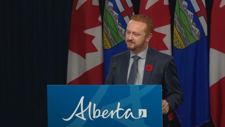 A man stands behind a podium with 'Alberta' written across the front.