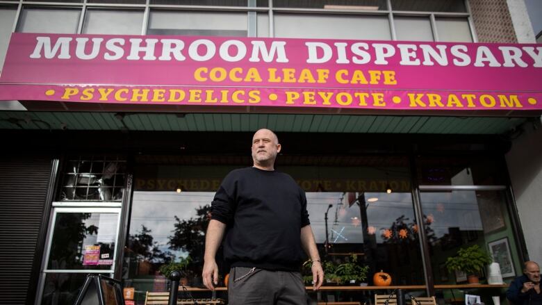 A man stands outside a storefront with a large pink awning that says Mushroom Dispensary on it.