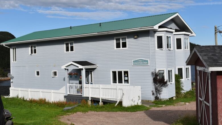 A grey two-storey building with a green roof. A sign on the side of the building reads 