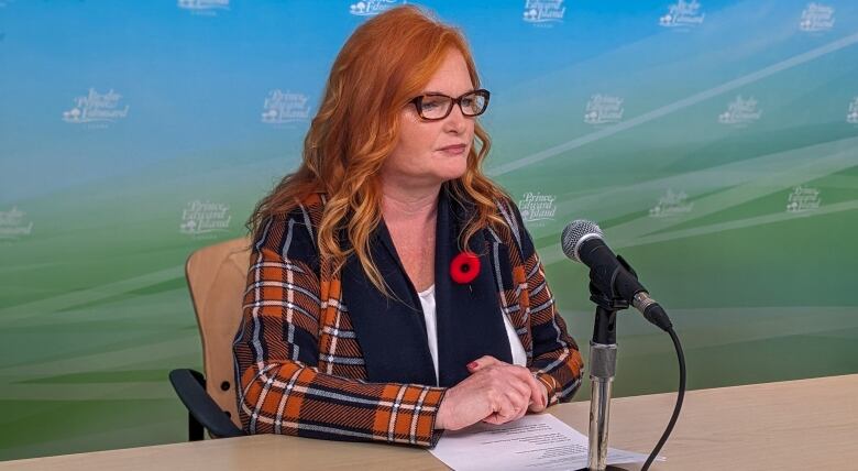 Woman with red hair, glasses and a poppy speaks into a microphone.