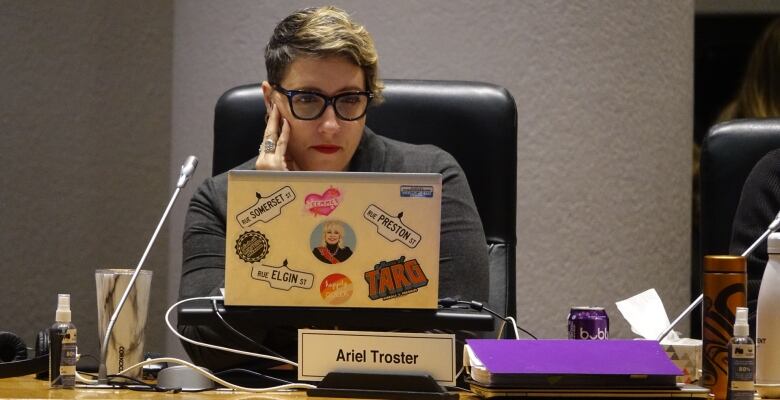 A women with short hair and glasses looks at a laptop decorated by stickers