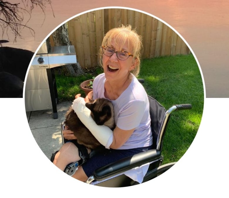 A woman in a wheelchair holds a cat and smiles.