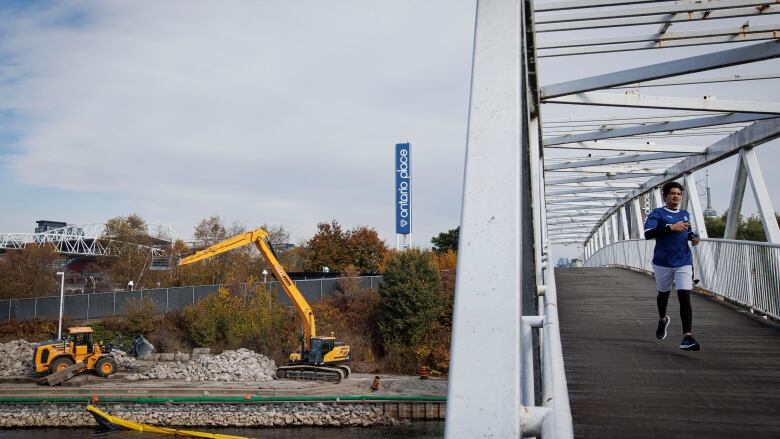 A runner strides along a bridge at Ontario Place, with construction in the background.