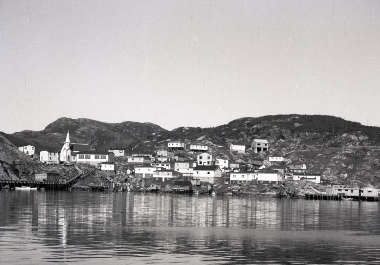 An old black and white image of a small town on the hills surrounding a body of water. At left can be seen a church steeple.