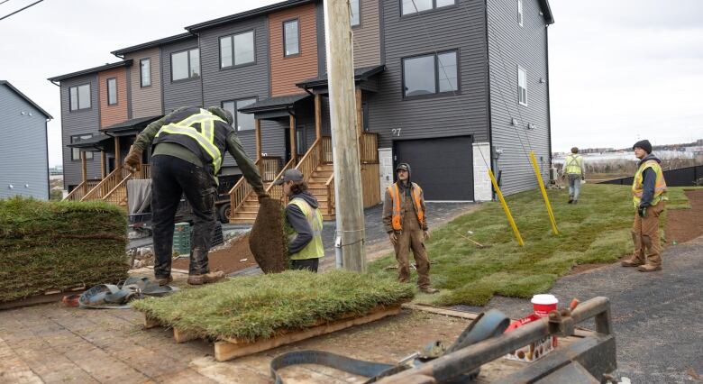 Workers in high visibility vests are seen in a line passing sod to each other to lay down in the yard of a home.