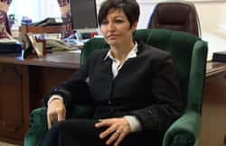 A woman with dark hair in a pixie cut sits in a green velvet chair.