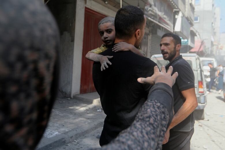 A woman reaches out for a child covered in dust as a man carries them away.