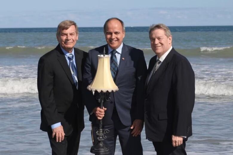 Three men stand on a beach holding a lamp