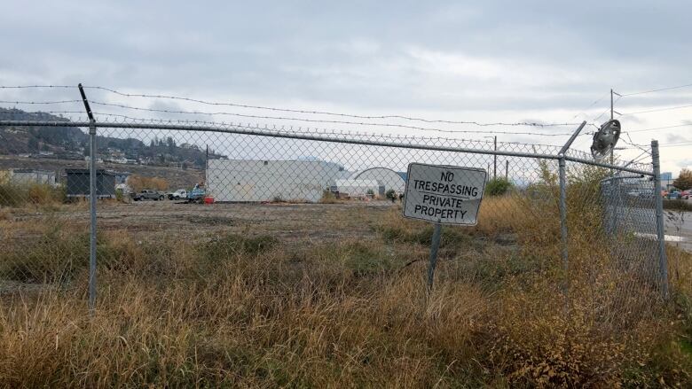 A  vacant lot in Kelowna surrounded by a large barbed wire fence with a No Trespassing / Private Property sign in the foreground. 