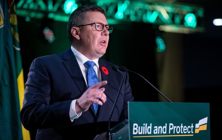 A man in a suit speaks at a podium, with a sign reading 