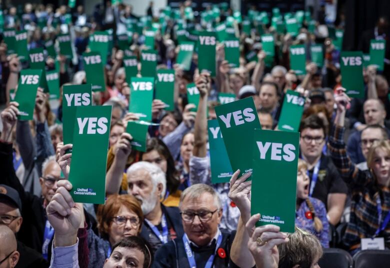 People hold up green cards while sitting on chairs.