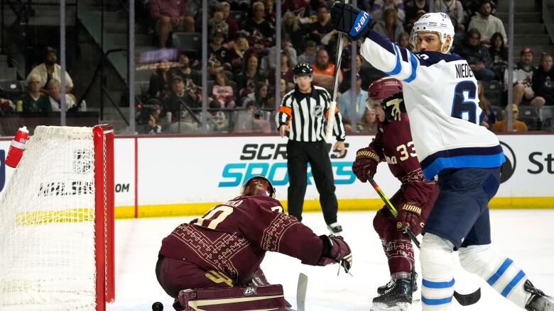 A male hockey player raises his hands to celebrate after scoring into the net.