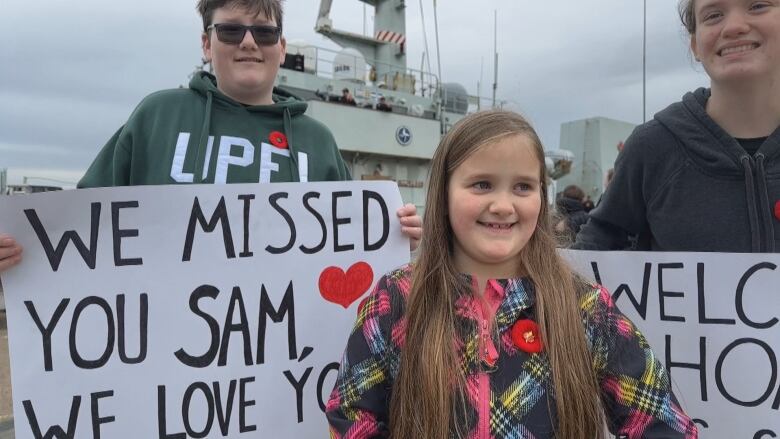 A young girl smiles as two adults stand behind her with signs saying 