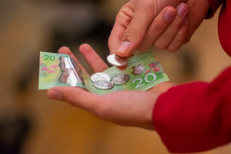 A person holding a $20 bill and 80 cents worth of change.