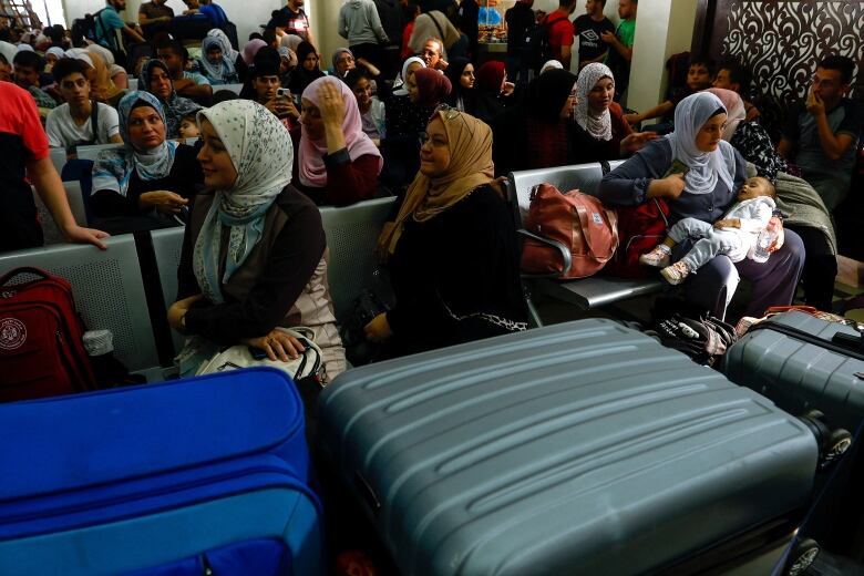 A number of people, mostly women, sitting down, with luggage in the foreground. 