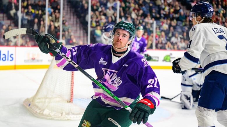 Hockey player holds stick up in front of crowd.