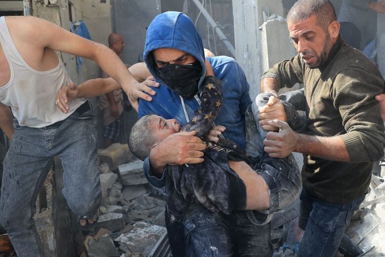 An injured child is carried out of a destroyed building by rescuers.