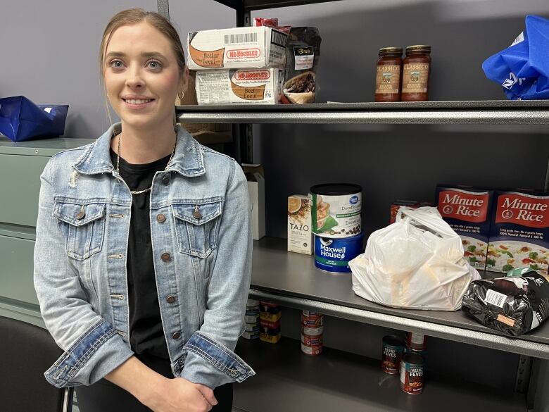 A woman stands in front of some food on shelves.